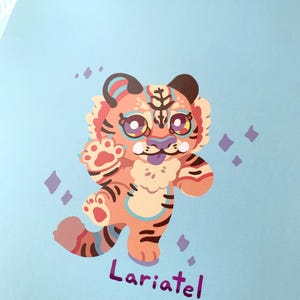 May include: A cartoon illustration of a tiger with orange and black stripes, blue and pink accents, and a purple tongue. The tiger is standing on a light blue background with purple and white sparkles. The text "Lariatel" is written in purple below the tiger.