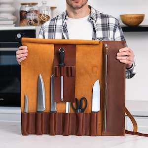 May include: A brown leather knife roll with multiple slots for knives and a sharpening steel. The roll is open and the knives are visible.