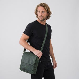 May include: A dark green leather messenger bag with a fold-over flap and an adjustable shoulder strap. The bag features a rectangular shape, a smooth matte finish, and metal hardware attachments for the strap, worn across the body.