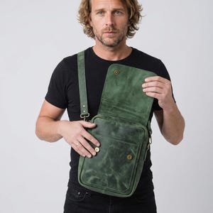 May include: A forest green leather crossbody bag featuring a rectangular silhouette, a fold-over flap with a snap closure, an adjustable shoulder strap, and a front pocket secured with two brass-toned metal snap buttons on a smooth leather surface.