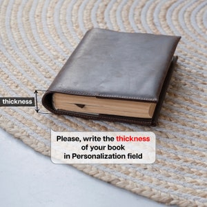 May include: A dark brown leather book cover enclosing a book with beige pages. A graphic overlay indicates the thickness of the book with an arrow and the text "thickness". A speech bubble contains the text "Please, write the thickness of your book in Personalization field".