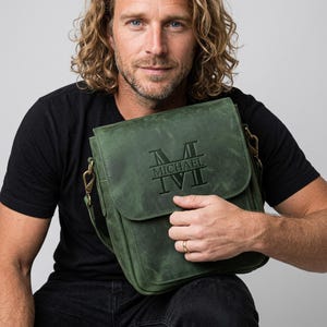 May include: A forest green leather messenger bag featuring a flap closure with an embossed monogram design. The center of the flap displays the name MICHAEL in a horizontal bar, flanked by the letter M above and the Roman numerals IV II below.