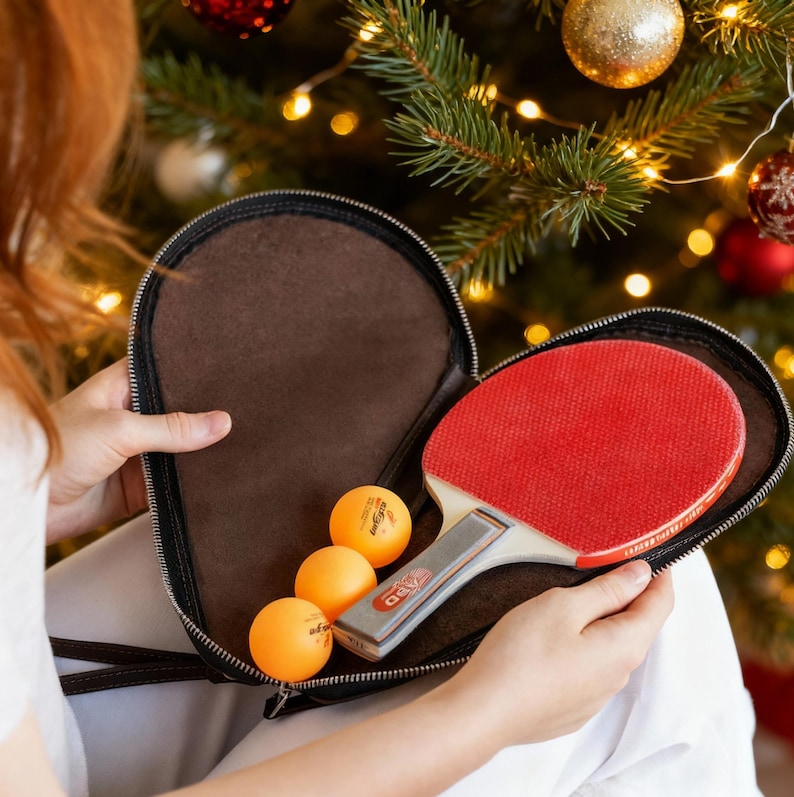 May include: A red ping pong paddle and three orange ping pong balls are in a black zippered case. The paddle has a wooden handle and a red rubber surface. The balls are a bright orange color. The case is brown inside.