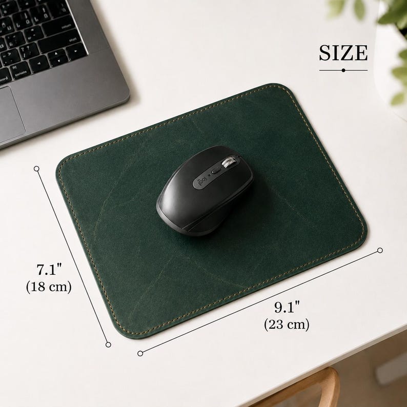 K&ouml;nnte beinhalten: Ein rechteckiges Mauspad aus dunkelgr&uuml;nem Leder mit sichtbaren N&auml;hten an den R&auml;ndern, auf dem eine schwarze kabellose Computermaus liegt. Die Ma&szlig;e sind deutlich mit 18 cm mal 23 cm angegeben und bieten eine klare Skalierung f&uuml;r das Produkt.