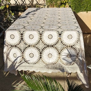 Peut inclure: Une nappe en crochet blanche avec un motif floral délicat. La nappe est posée sur une table et a un bord festonné.