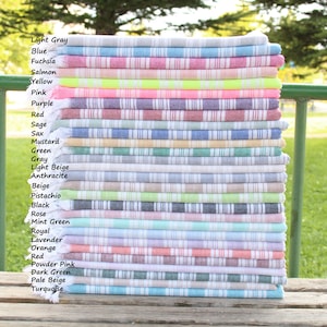 May include: A stack of 25 Turkish towels in various colours, including light grey, blue, fuchsia, salmon, yellow, pink, purple, red, sage, sax, mustard, green, grey, light beige, anthracite, beige, pistachio, black, rose, mint green, royal, lavender, orange, red, powder pink, dark green, pale beige, and turquoise.