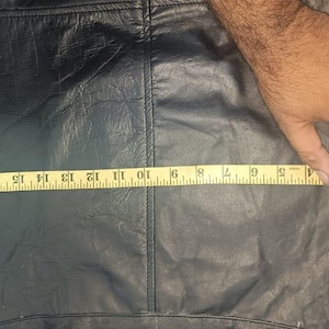 Może przedstawiać: Czarny sk&oacute;rzany element odzieży z miarką pokazującą długość około 48 cm. Sk&oacute;ra wydaje się miękka i ma widoczne szwy. Odzież jest mierzona przez rękę.