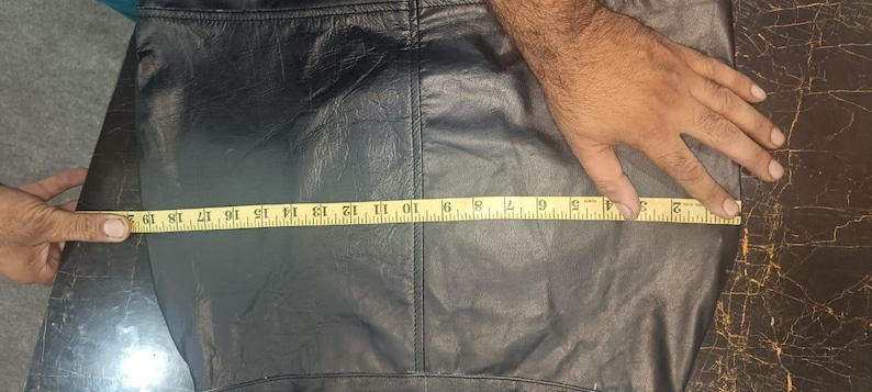 Może przedstawiać: Czarny sk&oacute;rzany element odzieży z miarką pokazującą długość około 48 cm. Sk&oacute;ra wydaje się miękka i ma widoczne szwy. Odzież jest mierzona przez rękę.