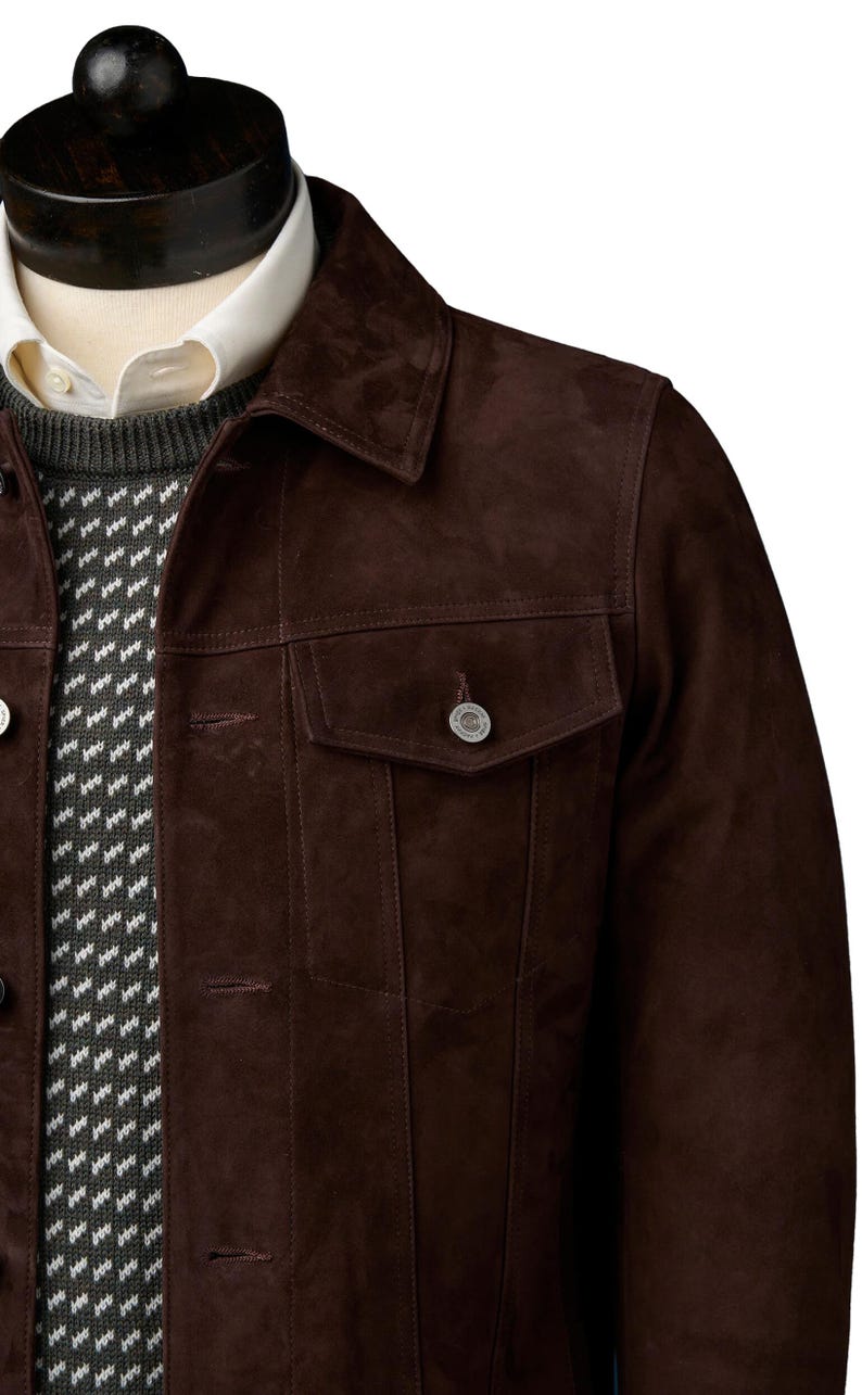 Op de afbeelding: Een bruin su&egrave;de jack met een knoopsluiting en een enkele borstzak. Het jack heeft een klassieke denim stijl.