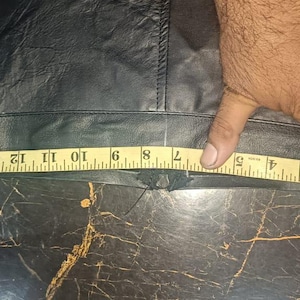 Może przedstawiać: Czarny sk&oacute;rzany element odzieży mierzony ż&oacute;łtą miarką. Taśma pokazuje pomiar około 40 cm. Odzież wydaje się być elementem odzieży, prawdopodobnie spodniami lub sp&oacute;dnicą, z widocznym szwem.