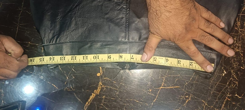 Może przedstawiać: Czarny sk&oacute;rzany element odzieży mierzony ż&oacute;łtą miarką. Taśma pokazuje pomiar około 40 cm. Odzież wydaje się być elementem odzieży, prawdopodobnie spodniami lub sp&oacute;dnicą, z widocznym szwem.