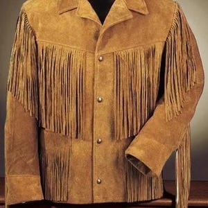 May include: A tan suede jacket with long fringe detailing on the chest, sleeves, and back. The jacket has a collared neckline, button-down closure, and two front pockets. The jacket is a western-style garment.