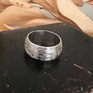 Puede incluir: Un anillo de plata con un acabado texturizado y martillado. El anillo es ancho y tiene una forma redondeada.