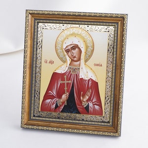 May include: A framed icon of Saint Sophia, a religious figure, with a gold and silver frame. The icon depicts Saint Sophia in a red robe with a cross in her hand. The text "Св. София" is written in Cyrillic script at the top of the icon.
