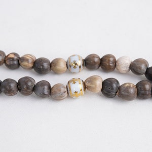 May include: A strand of brown wooden beads with two white beads with gold accents.