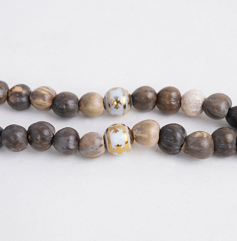 May include: A strand of brown wooden beads with two white beads with gold accents.