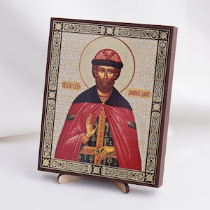 May include: A wooden icon of a religious figure with a red and black robe, a gold crown, and a gold background. The icon is framed in a dark wood frame with gold accents. The text "СЕГОДНЯ КНЯЗЬ" and "ДМИТРИЙ ДОНЕ" is visible on the icon.