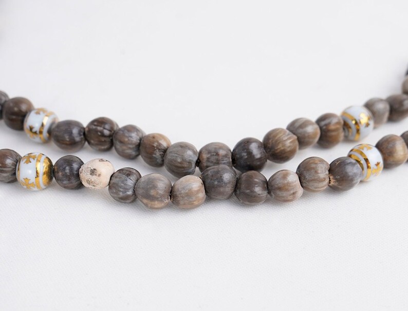 May include: A brown and white beaded necklace with gold accents. The beads are made from natural materials and have a rustic look.