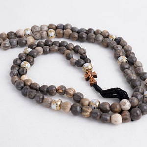 May include: A brown wooden prayer beads necklace with a small wooden cross charm. The beads are interspersed with white beads with gold accents.