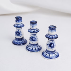 Peut inclure: Trois bougeoirs en céramique blanche avec des motifs floraux bleus et blancs. Les bougeoirs sont alignés sur une surface blanche.