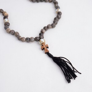 May include: A brown wooden rosary with a small wooden cross and a black tassel. The beads are made of natural wood and have a rustic look.