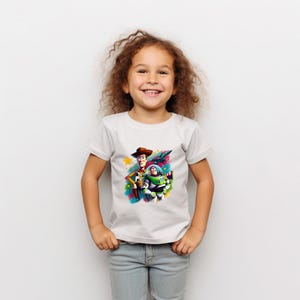 May include: A white t-shirt with a vibrant graphic of Woody and Buzz Lightyear from Toy Story. The design includes a star and a jet. The shirt is being worn by a young child.