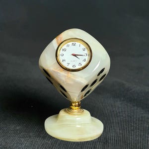 May include: A white marble clock shaped like a dice with black dots on each side. The clock face is white with black numbers and hands. The clock is on a white marble base.