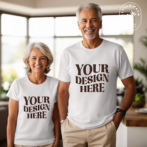 Puede incluir: Dos personas con camisetas blancas con el texto "YOUR DESIGN HERE" impreso en marrón en la parte delantera. Las camisetas son una maqueta para un diseño personalizado.