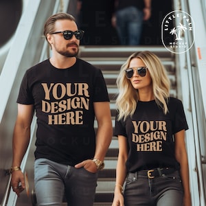 Pode incluir: Duas pessoas vestindo camisetas pretas com o texto "Your Design Here" impresso em marrom na frente. O casal est&aacute; em p&eacute; em uma escada.