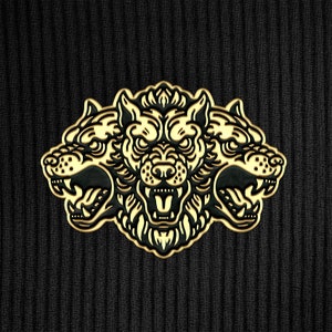 Puede incluir: Un pin de metal dorado con un diseño de lobo de tres cabezas. Cada cabeza de lobo tiene una expresión de gruñido con dientes afilados y un patrón de pelaje detallado.