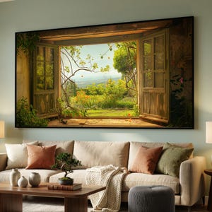 Puede incluir: Una obra de arte enmarcada representa una ventana abierta con vistas a una vibrante escena de jardín. El marco de la ventana es de madera envejecida, y el jardín presenta exuberante vegetación, flores coloridas y un paisaje distante bajo un cielo brillante. La obra se exhibe sobre un sofá beige.
