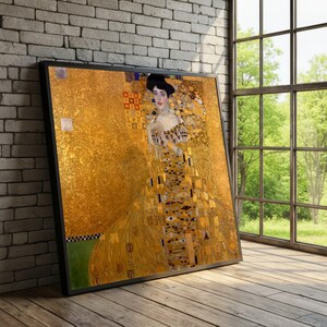 Puede incluir: Impresión enmarcada del "Retrato de Adele Bloch-Bauer I" de Gustav Klimt. La obra de arte presenta a una mujer con un vestido dorado con patrones y detalles intrincados. La impresión se muestra contra una pared de ladrillo y un suelo de madera.