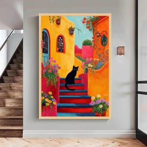 May include: A colourful painting shows a black cat on steps leading to a yellow building. The steps are red and blue, and the scene is filled with flowers. The artwork is framed in a light wood, with orange and red hues.
