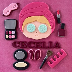 May include: A collection of pink, beige, and black cosmetic-themed decorations. Includes a face with cucumber slices on the eyes, a sleep mask, eyeshadow, lipstick, nail polish, a makeup brush, and the name "CECILIA" with the number "10".