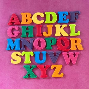 May include: Colorful alphabet letters in various shades of red, orange, yellow, green, blue, and purple are arranged on a pink background. The letters are in a bold, rounded font, perfect for educational or decorative purposes.