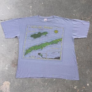May include: A light purple short-sleeve t-shirt featuring a large graphic print of a map titled The Bay Islands of Honduras. The design includes a compass rose, detailed island topography in green, and a smaller inset map of the region.