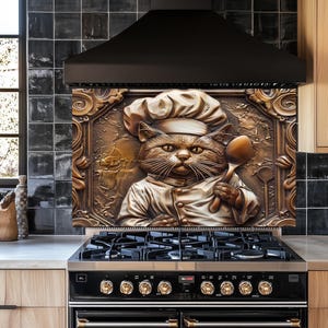 May include: A bronze-colored relief sculpture of a cat chef holding a spoon, set above a black gas range. The cat wears a chef's hat and uniform, framed by an ornate border. The kitchen features black tile backsplash and light wood cabinetry.