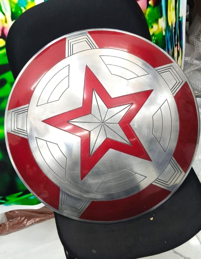 May include: A red and silver Captain America shield with a five-pointed star in the center. The shield has a raised, textured surface.