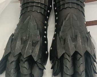 Könnte beinhalten: Ein Paar schwarze Lederhandschuhe mit Metallplatten und Nieten. Die Handschuhe haben ein stacheliges Design und werden an den Händen getragen.