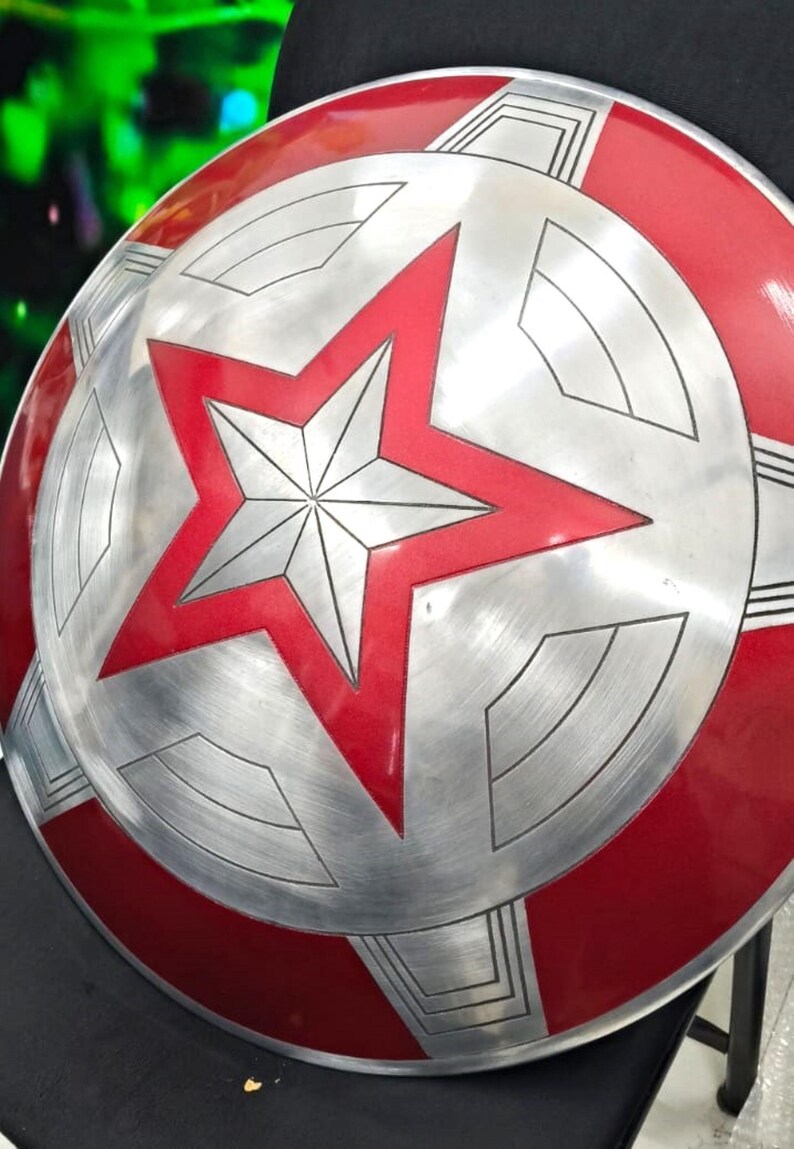 May include: A red and silver Captain America shield with a five-pointed star in the center. The shield is made of metal and has a textured surface.