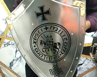 May include: A silver shield with a black cross and a black circular emblem with the text "XPSTI MILITVM BIS.IAM" and a knight on horseback. The shield has gold accents and rivets.