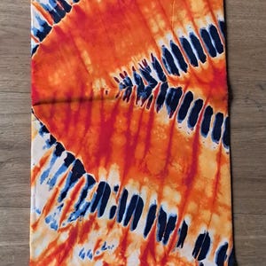 Peut inclure: Un textile vibrant avec un motif tie-dye dans les tons orange, blanc et bleu. Le tissu présente un motif répétitif de lignes courbes et de taches. Le texte "PRINTED BY SUPER RR WAX" est visible.