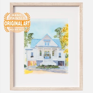 May include: A framed watercolor painting of a white house with a blue roof, blue doors, and a front porch. The artwork features green and yellow trees, a light blue sky, and a circular orange stamp that reads HAND PAINTED ORIGINAL ART NO PRINTS.
