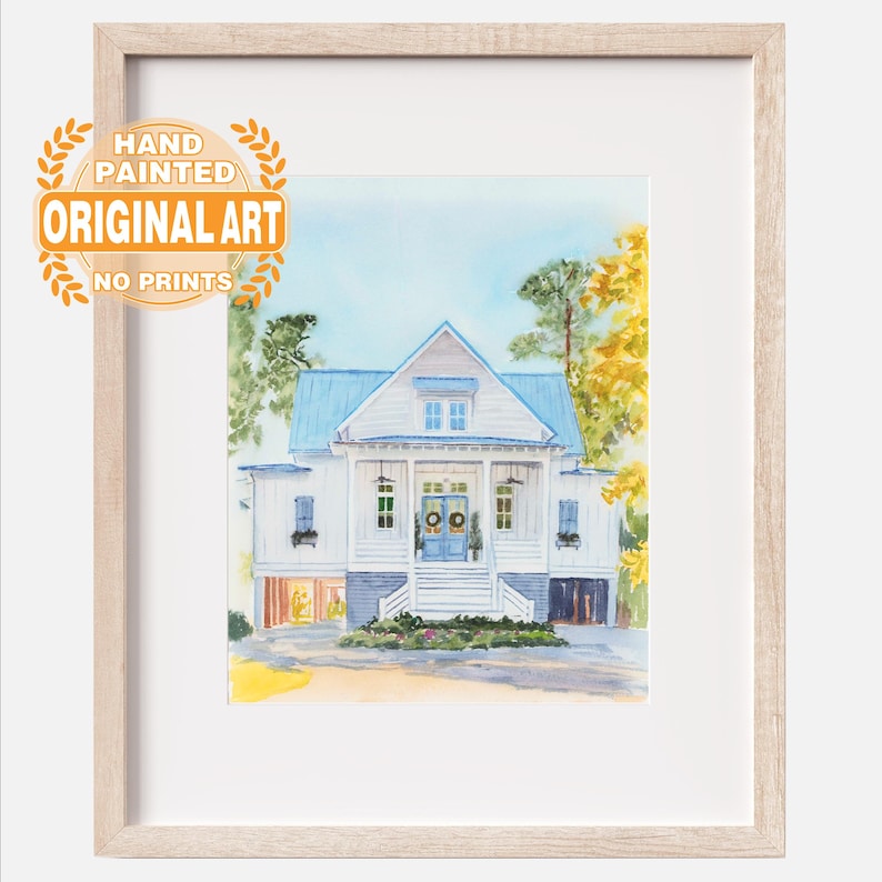 May include: A framed watercolor painting of a white house with a blue roof, blue doors, and a front porch. The artwork features green and yellow trees, a light blue sky, and a circular orange stamp that reads HAND PAINTED ORIGINAL ART NO PRINTS.