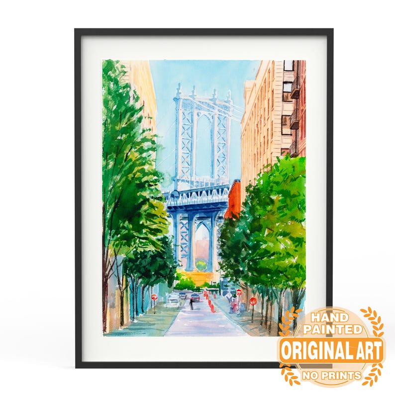May include: Framed watercolor painting of the Manhattan Bridge in New York City. The artwork features a blue bridge, buildings, and green trees lining a street. The painting is in a black frame and includes text that reads "Hand Painted Original Art No Prints."