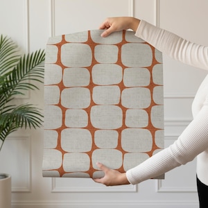 May include: A roll of wallpaper featuring a repeating geometric pattern of rounded light gray squares separated by a vibrant burnt orange grid. The design has a subtle textured appearance across the surface of the paper material.