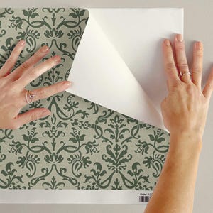 A person's hands are shown placing a piece of paper over a patterned wallpaper, with the paper partially covering the wallpaper.