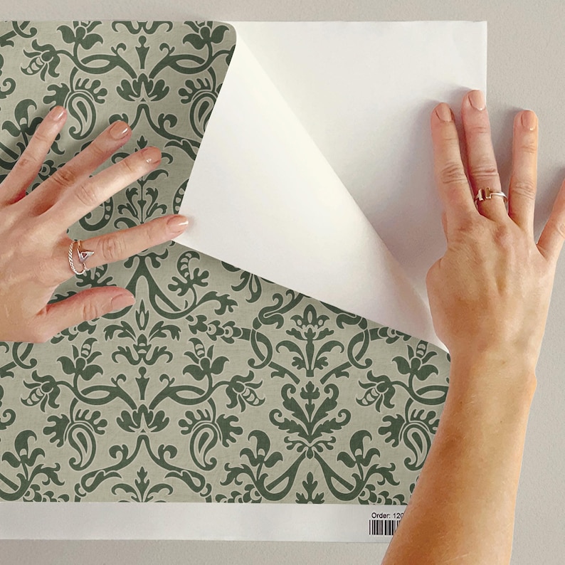 A person's hands are shown placing a piece of paper over a patterned wallpaper, with the paper partially covering the wallpaper.