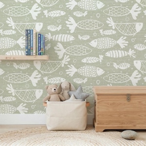 Könnte beinhalten: Hellgrüne Wand mit sich wiederholendem weißen Fischmuster. Ein Holzregal hält Bücher. Ein Leinwandkorb mit Holzgriffen enthält Stofftiere. Eine Holzkiste befindet sich rechts. Ein runder Teppich liegt auf dem Boden.