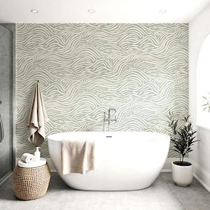 Puede incluir: Un baño moderno con una bañera ovalada blanca, una mesita auxiliar tejida y una planta en maceta. La pared presenta un patrón de ondas en verde claro y blanco. Una toalla beige cuelga y otra descansa sobre la bañera.